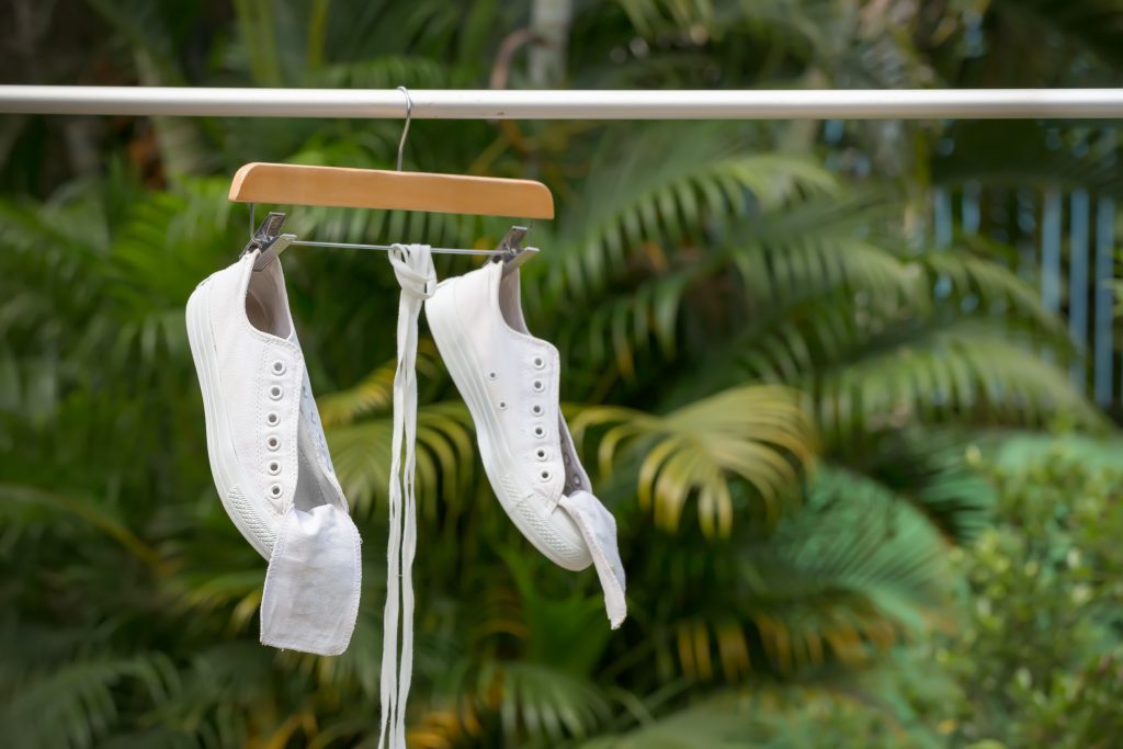 White sneakers hanging on clothesline with hanger in the sun.