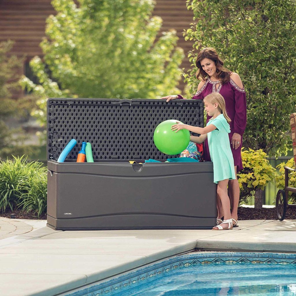 A woman watches on as a girl places a ball into large storage bench