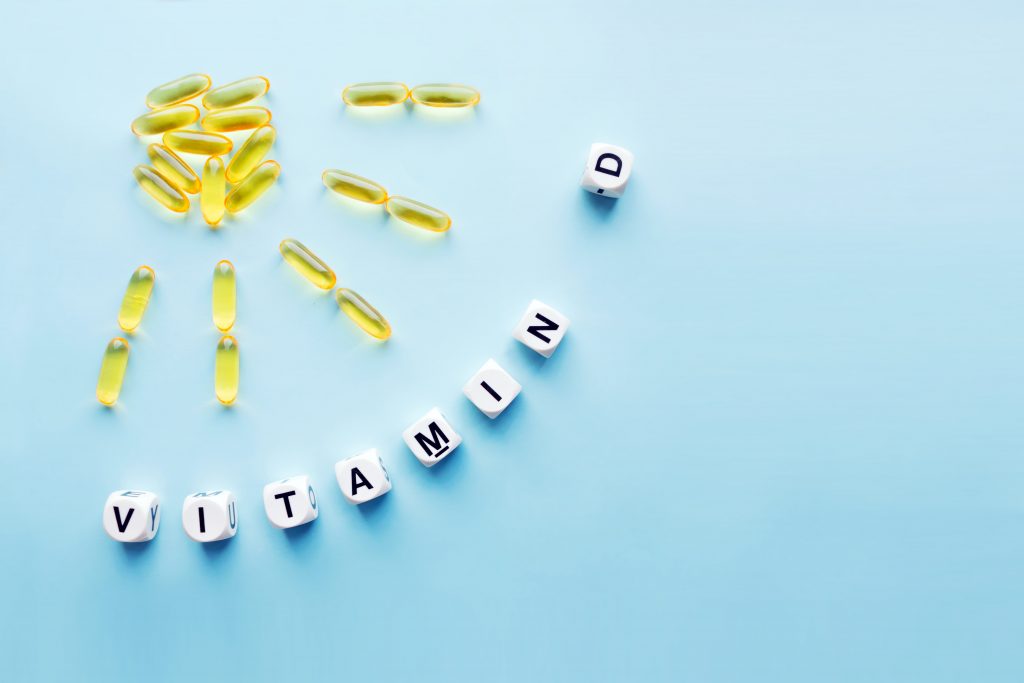 Yellow capsules in the form of the sun with rays and the word vitamin D from white cubes with letters on a blue background. VITAMIN D word for he