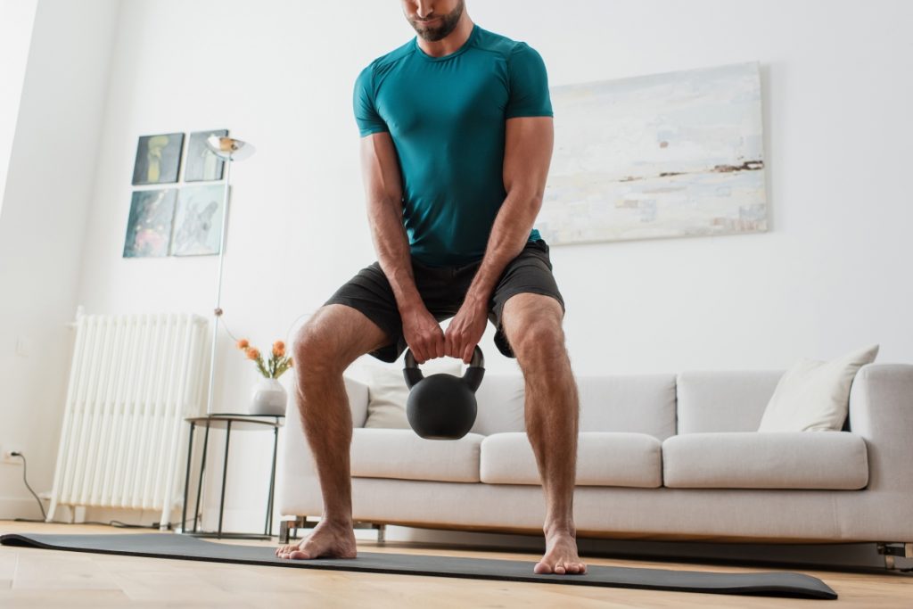 cropped view of barefoot man lifting kettlebell at home