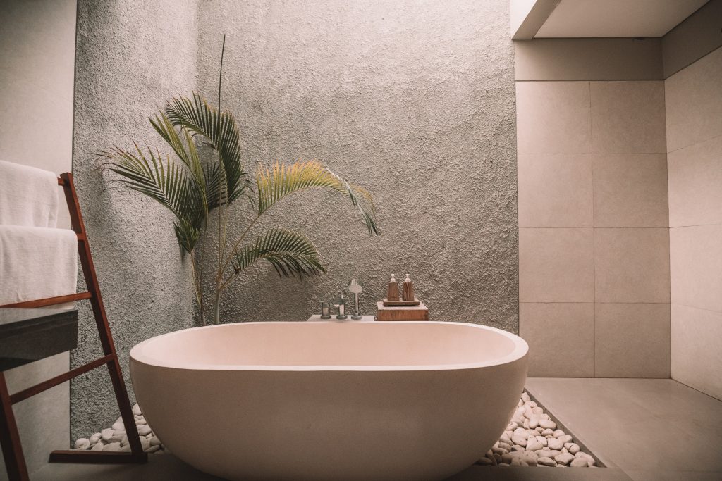 Japandi bathroom with bathtub and textured walls, plants, stones, and accessories